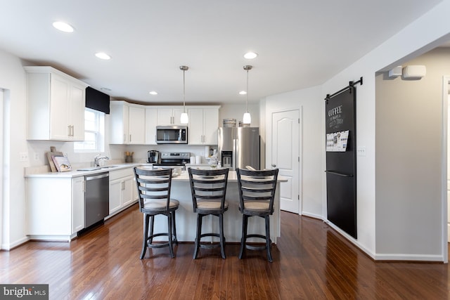 kitchen featuring appliances with stainless steel finishes, a barn door, decorative light fixtures, white cabinets, and a kitchen island