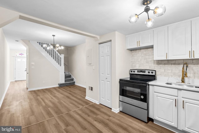 kitchen featuring stainless steel electric range, sink, light hardwood / wood-style floors, white cabinetry, and a chandelier