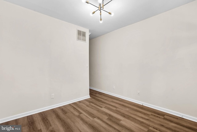 empty room with hardwood / wood-style flooring and a notable chandelier