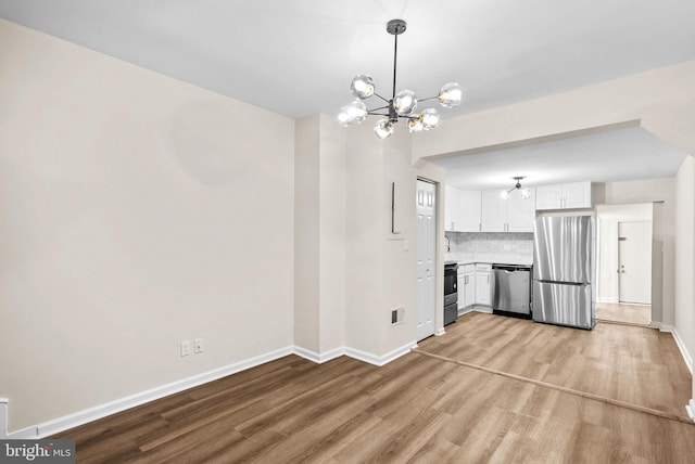 kitchen featuring decorative backsplash, light hardwood / wood-style floors, white cabinetry, stainless steel appliances, and a chandelier