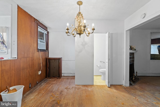 unfurnished dining area featuring baseboard heating, a fireplace, hardwood / wood-style floors, and a chandelier