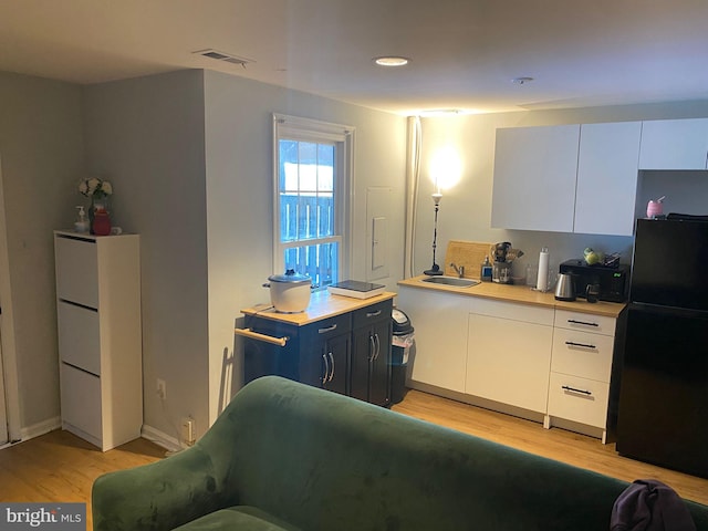 kitchen with black refrigerator, sink, blue cabinetry, light hardwood / wood-style flooring, and white cabinetry