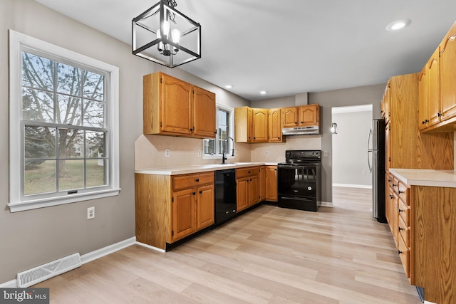 kitchen featuring decorative light fixtures, a wealth of natural light, light hardwood / wood-style flooring, and black appliances