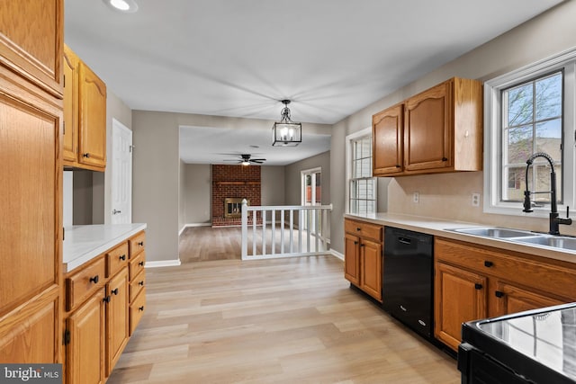 kitchen featuring sink, decorative light fixtures, a brick fireplace, light wood-type flooring, and black appliances