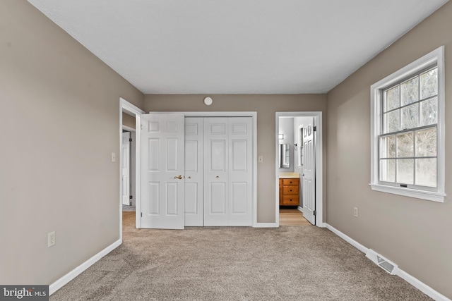 unfurnished bedroom with a closet, ensuite bathroom, and light carpet