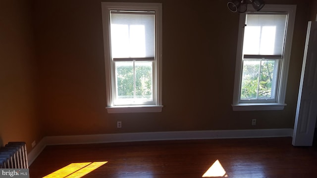 unfurnished room with radiator heating unit, dark wood-type flooring, and plenty of natural light