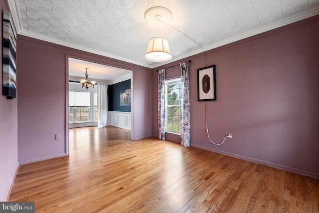 spare room with a chandelier, light wood-type flooring, and ornamental molding