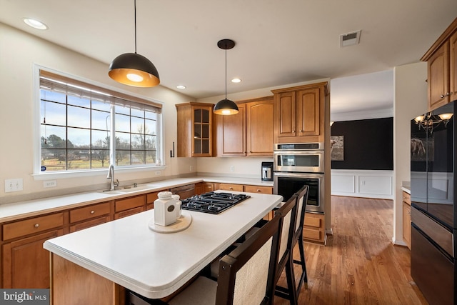 kitchen featuring stainless steel appliances, sink, wood-type flooring, a kitchen island, and hanging light fixtures