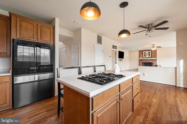 kitchen featuring ceiling fan, stainless steel gas cooktop, hardwood / wood-style floors, a breakfast bar area, and a fireplace