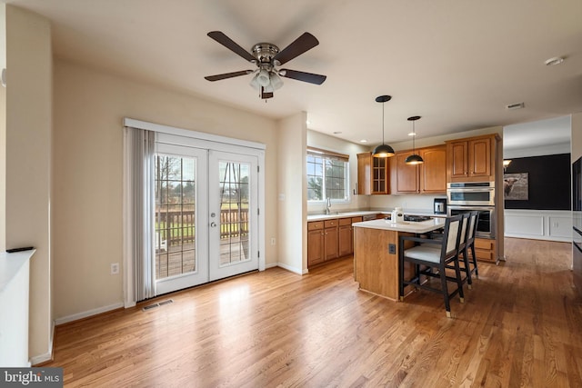 kitchen featuring french doors, hanging light fixtures, light hardwood / wood-style flooring, a kitchen bar, and a kitchen island