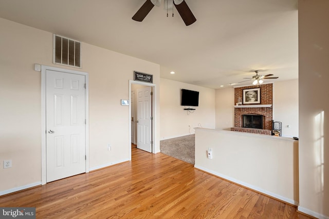 unfurnished living room featuring ceiling fan, light wood-type flooring, and a fireplace