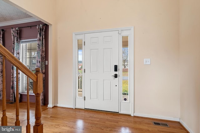 foyer entrance with ornamental molding, a healthy amount of sunlight, and light wood-type flooring