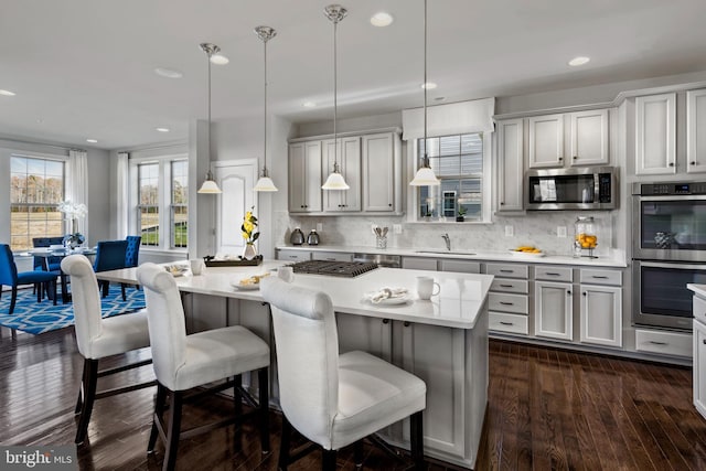 kitchen with tasteful backsplash, stainless steel appliances, decorative light fixtures, a center island, and dark hardwood / wood-style floors