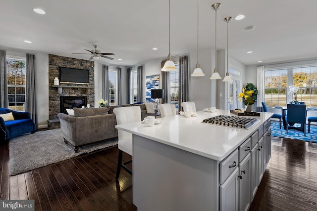 kitchen with a center island, a kitchen breakfast bar, hanging light fixtures, a fireplace, and stainless steel gas cooktop