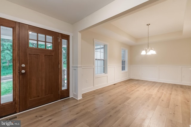 foyer entrance with a raised ceiling, light hardwood / wood-style floors, and an inviting chandelier