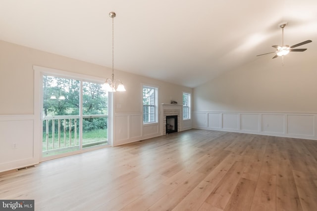 unfurnished living room featuring ceiling fan with notable chandelier, light wood-type flooring, a brick fireplace, and vaulted ceiling