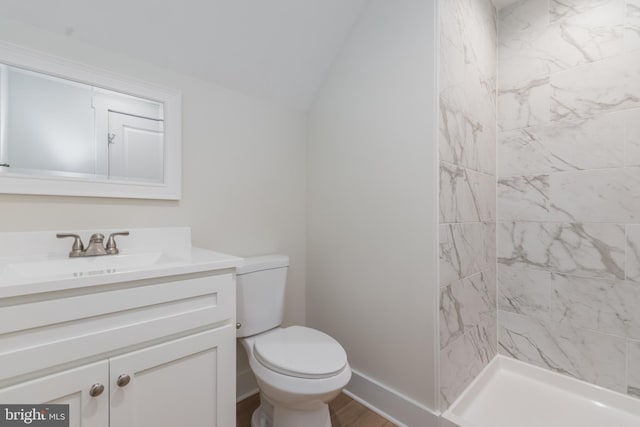 bathroom with vanity, vaulted ceiling, tiled shower, hardwood / wood-style flooring, and toilet