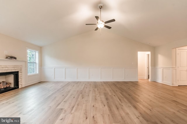 unfurnished living room with a brick fireplace, ceiling fan, vaulted ceiling, and light wood-type flooring