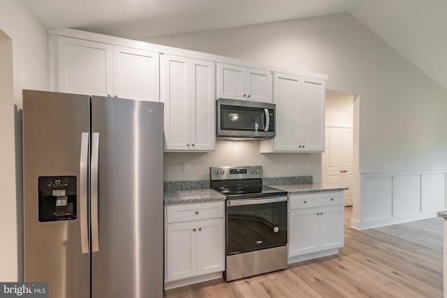 kitchen with light stone countertops, appliances with stainless steel finishes, lofted ceiling, white cabinets, and light wood-type flooring