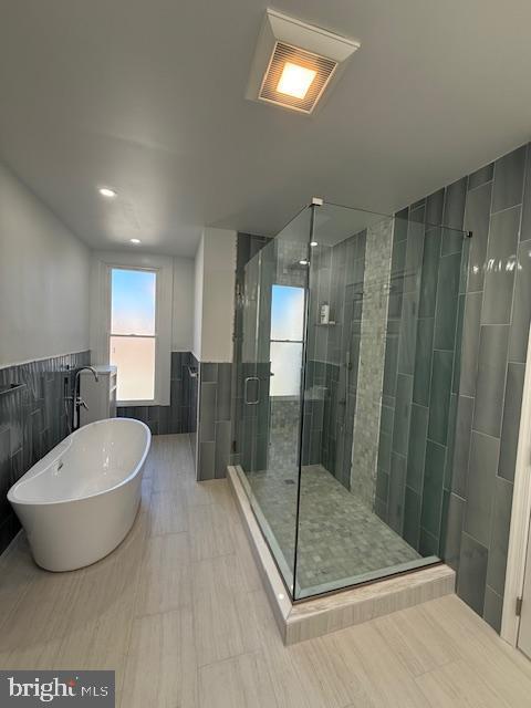 bathroom with shower with separate bathtub and tile walls