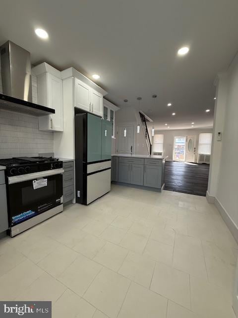 kitchen with decorative backsplash, appliances with stainless steel finishes, white cabinetry, and wall chimney range hood