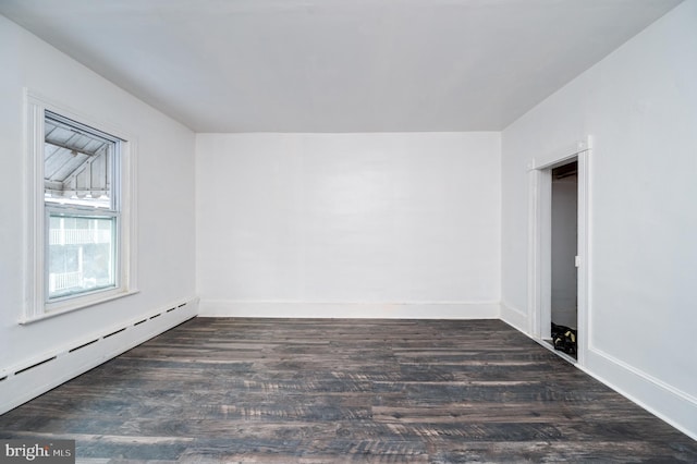 spare room featuring baseboards, baseboard heating, and dark wood-type flooring