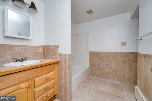 bathroom with a washtub, tile walls, a baseboard radiator, visible vents, and tile patterned floors