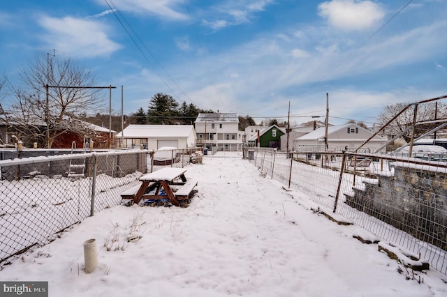 yard layered in snow with a detached garage, fence, and a residential view