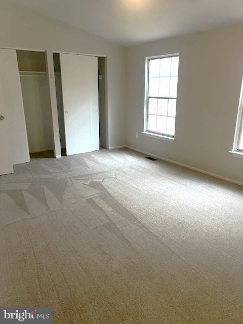 unfurnished bedroom featuring light carpet and multiple closets