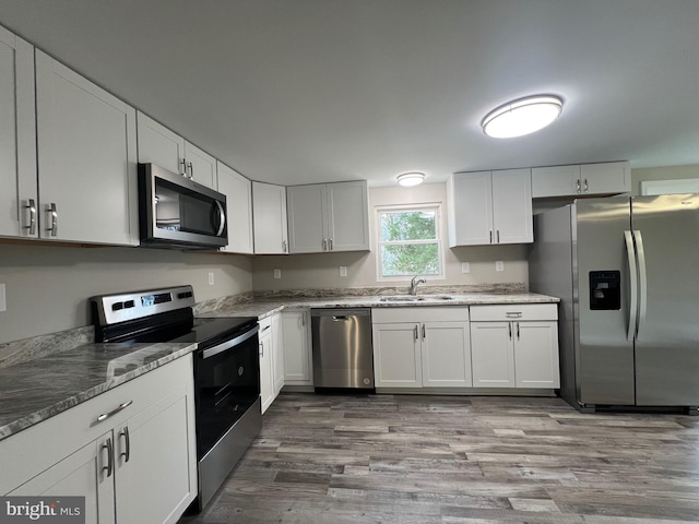 kitchen with sink, dark stone countertops, light hardwood / wood-style floors, white cabinets, and appliances with stainless steel finishes