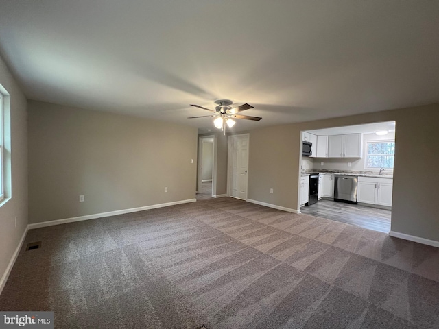 unfurnished living room with ceiling fan, carpet floors, and sink