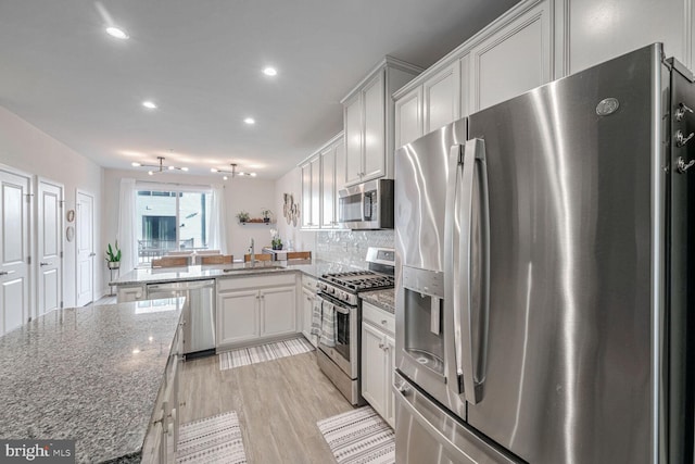 kitchen featuring sink, backsplash, kitchen peninsula, dark stone counters, and appliances with stainless steel finishes