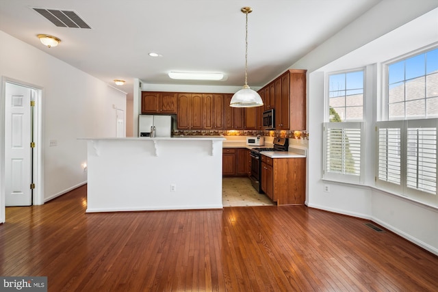 kitchen with hardwood / wood-style flooring, stainless steel appliances, tasteful backsplash, hanging light fixtures, and a center island