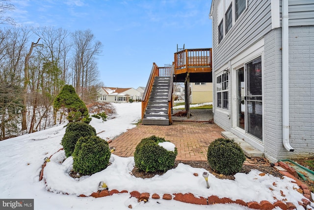 snowy yard featuring a wooden deck and a patio area