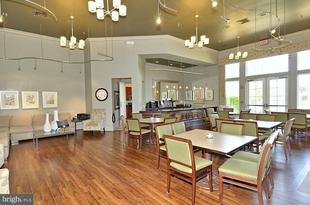 dining space featuring a towering ceiling, hardwood / wood-style flooring, crown molding, and a chandelier