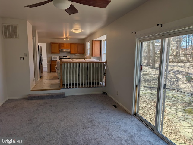 unfurnished living room featuring baseboards, visible vents, ceiling fan, and light colored carpet