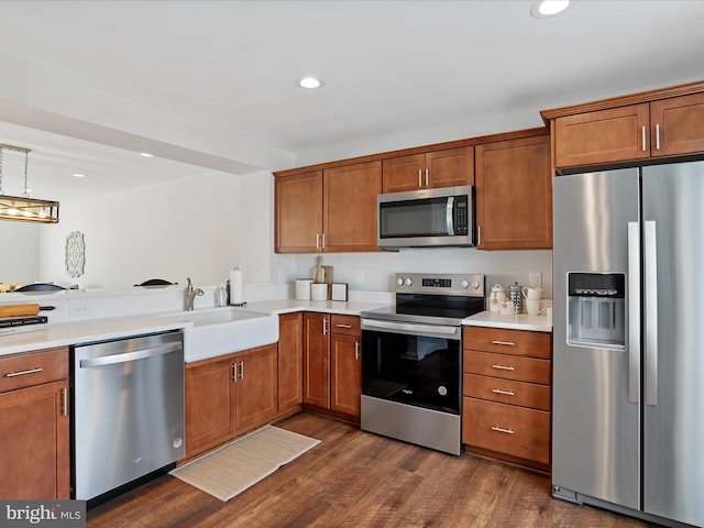 kitchen featuring appliances with stainless steel finishes, sink, hanging light fixtures, dark hardwood / wood-style floors, and kitchen peninsula