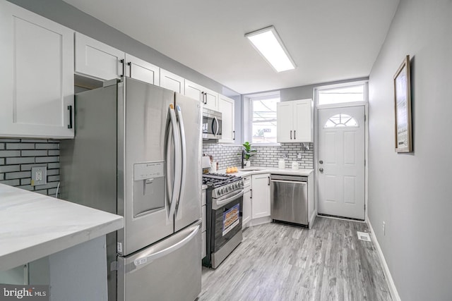 kitchen with white cabinets, light hardwood / wood-style floors, stainless steel appliances, and tasteful backsplash