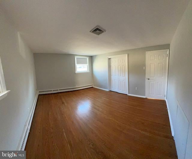 unfurnished bedroom with dark hardwood / wood-style flooring and baseboard heating