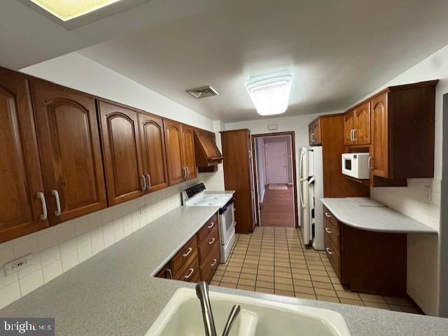 kitchen with custom exhaust hood, white appliances, sink, light tile patterned floors, and lofted ceiling