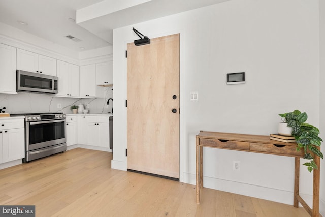 kitchen featuring sink, light hardwood / wood-style flooring, tasteful backsplash, white cabinetry, and stainless steel appliances