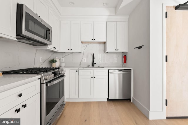 kitchen with light stone counters, stainless steel appliances, sink, white cabinets, and light hardwood / wood-style floors