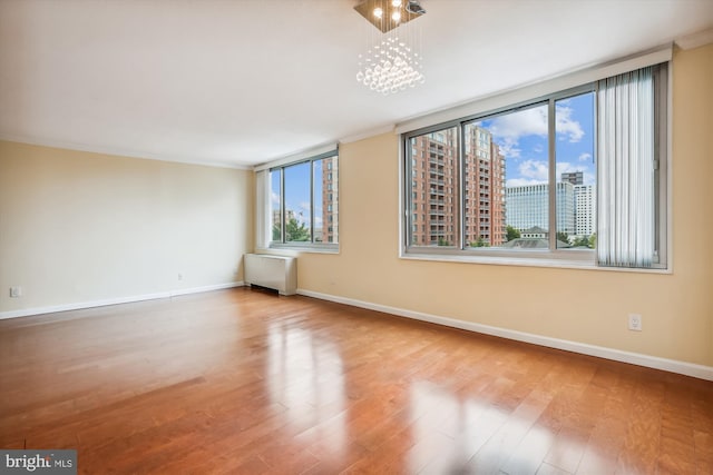 spare room with hardwood / wood-style flooring, ornamental molding, radiator, and a chandelier