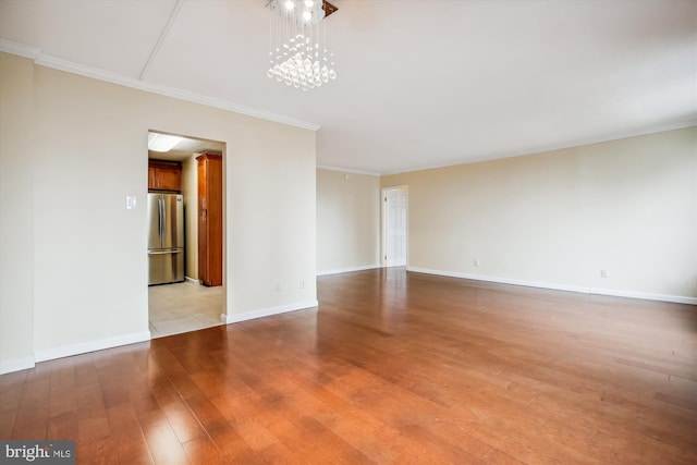 spare room with light wood-type flooring, ornamental molding, and a chandelier