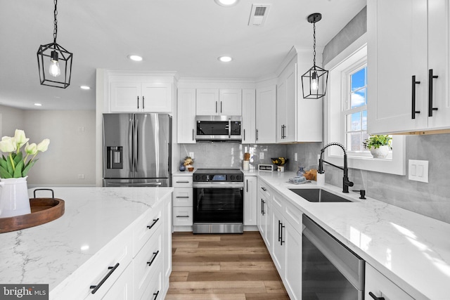 kitchen featuring stainless steel appliances, sink, pendant lighting, wood-type flooring, and white cabinets