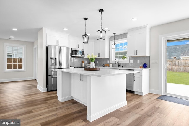 kitchen featuring pendant lighting, white cabinets, light hardwood / wood-style flooring, appliances with stainless steel finishes, and a kitchen island