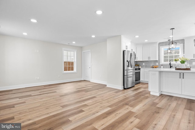 kitchen with a wealth of natural light, white cabinetry, stainless steel appliances, pendant lighting, and light wood-type flooring