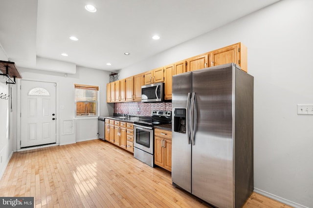 kitchen with appliances with stainless steel finishes, backsplash, sink, light brown cabinets, and light hardwood / wood-style flooring