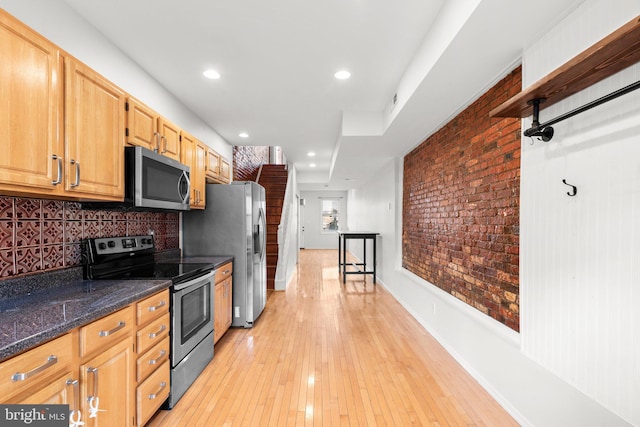 kitchen with backsplash, stainless steel appliances, light hardwood / wood-style flooring, and dark stone countertops