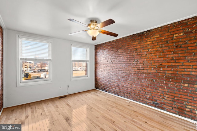 unfurnished room featuring light wood-type flooring, ceiling fan, and brick wall